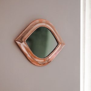 small copper mirror fixed to a plaster coloured wall
