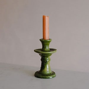 small green ceramic candlestick with an orange st eval candle in