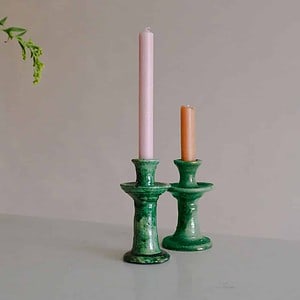two green tamegroute candlesticks on marble backdrop holding a pink and an orange dinner candles